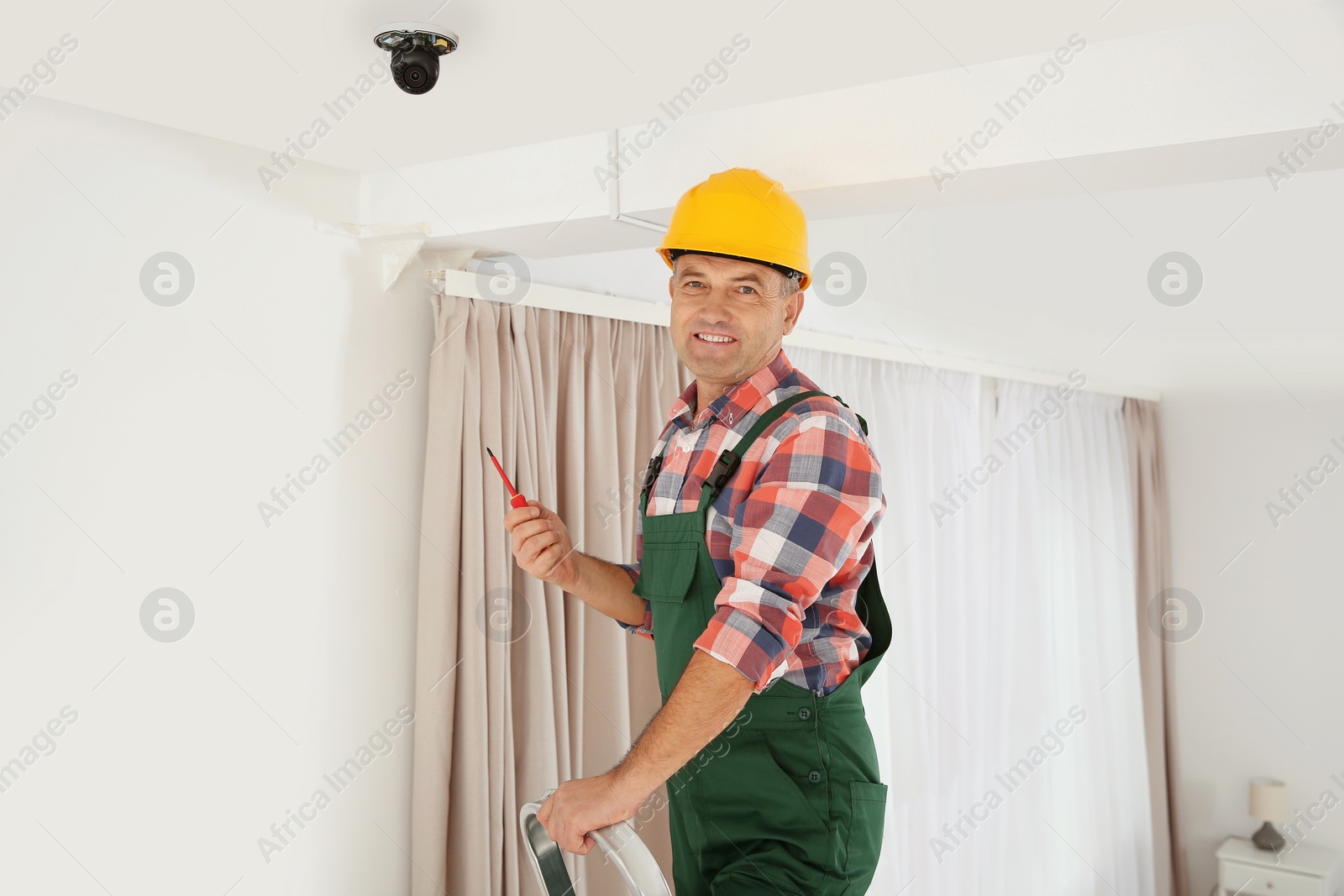 Photo of Electrician with screwdriver repairing CCTV camera indoors