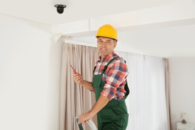 Electrician with screwdriver repairing CCTV camera indoors