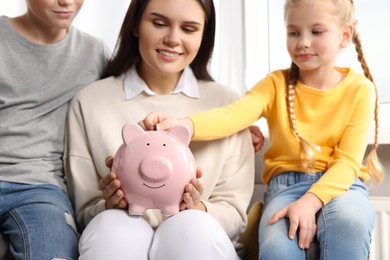 Photo of Happy family putting coin into piggy bank at home, closeup