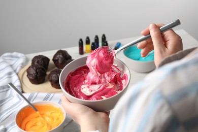 Photo of Woman mixing pink food coloring indoors, closeup. Decorate cupcakes