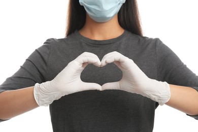 Photo of Woman in protective face mask and medical gloves making heart with hands on white background, closeup