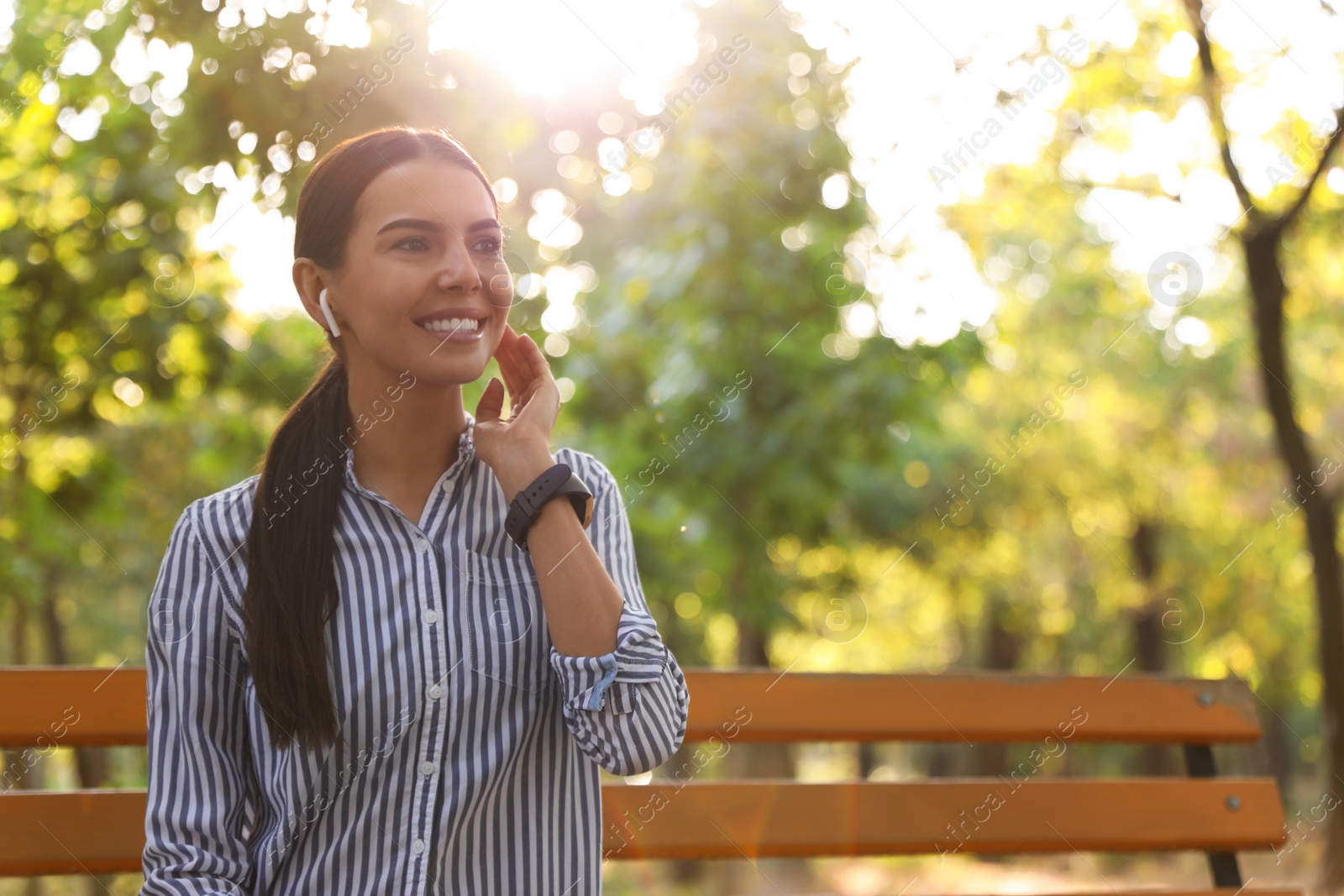 Photo of Young woman with wireless earphones in park