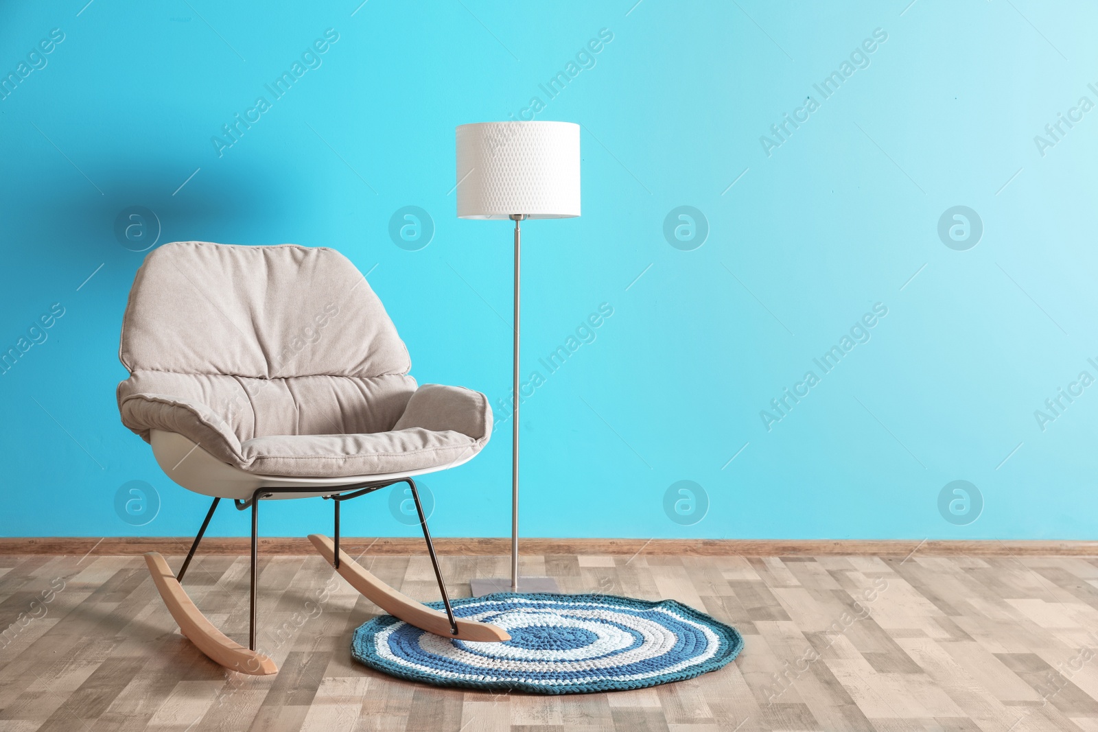 Photo of Comfortable armchair, small rug and white floor lamp against color wall