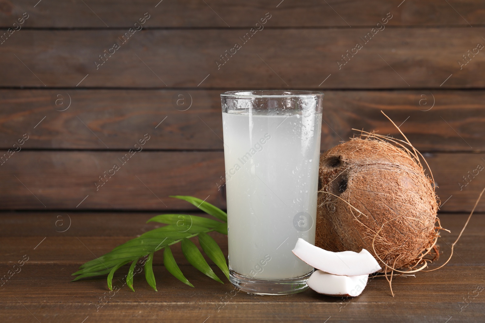 Photo of Glass of coconut water, leaf and nuts on wooden table, space for text