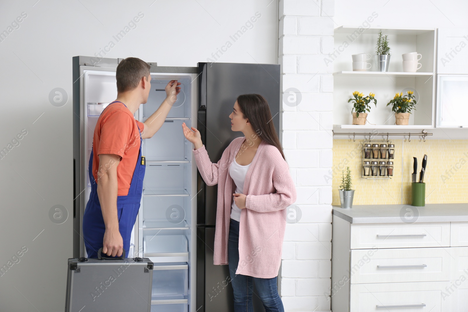 Photo of Male technician talking with client near refrigerator in kitchen