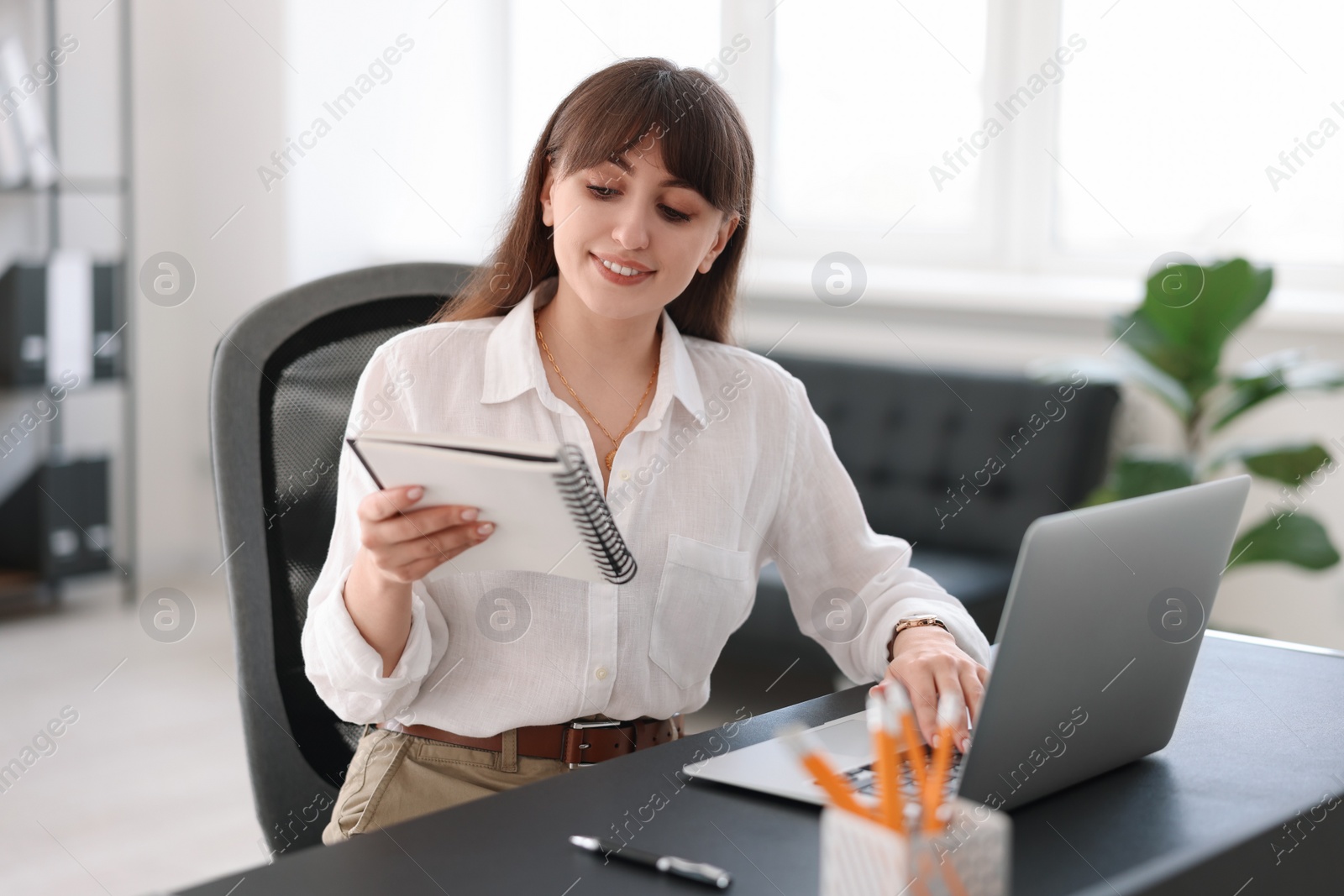 Photo of Woman with notebook watching webinar at table in office