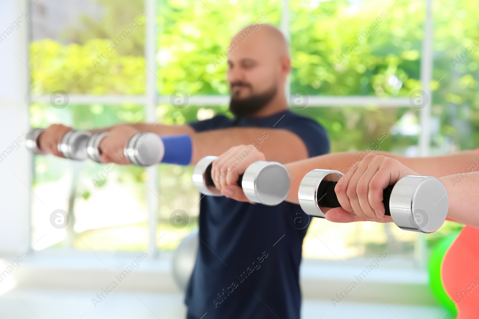 Photo of Overweight man and woman doing exercise with dumbbells in gym