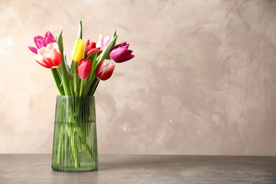 Photo of Beautiful spring tulips in vase on table against light background. Space for text
