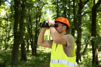 Forester with binoculars examining plants in forest