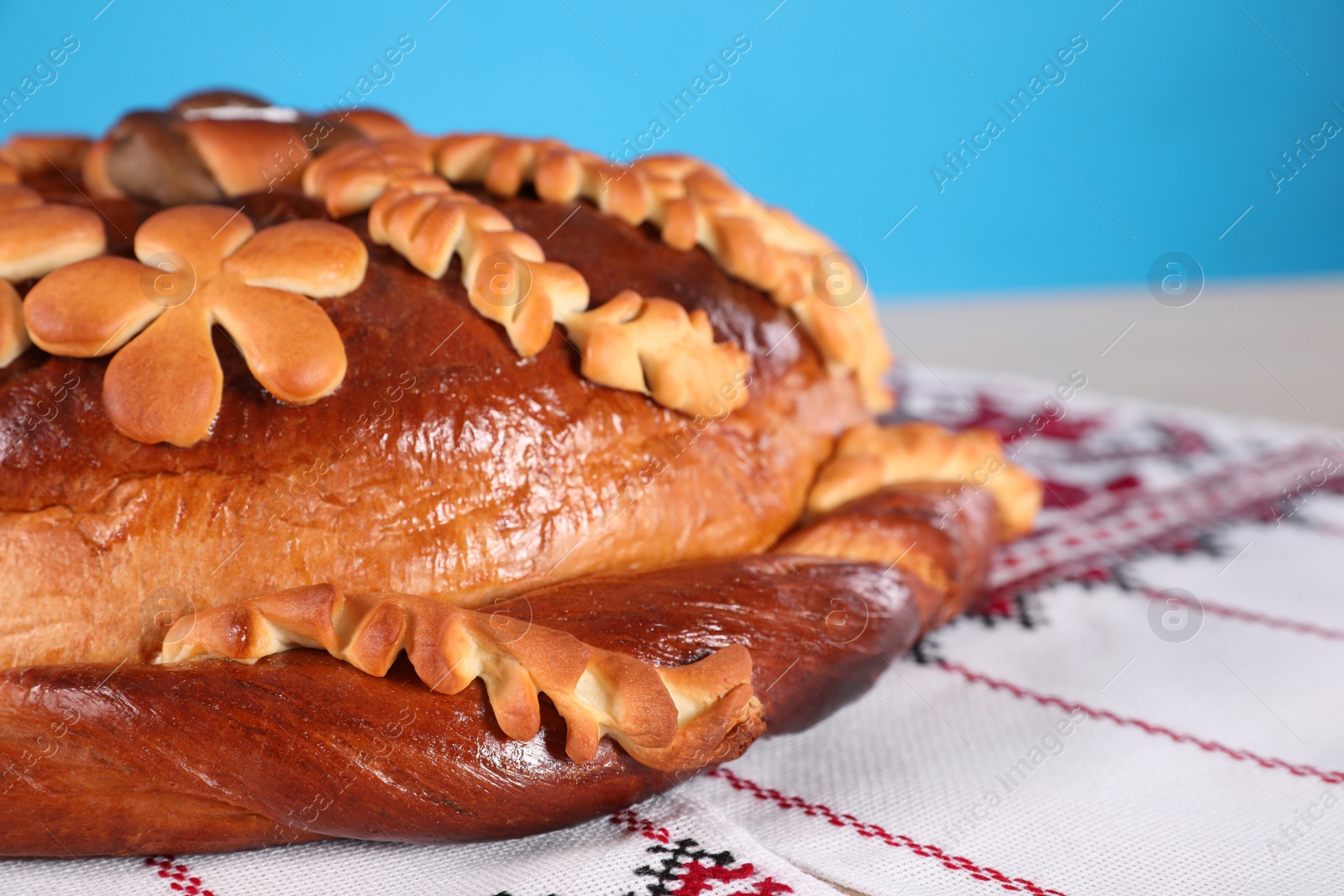 Photo of Rushnyk with korovai on light blue background, closeup. Ukrainian bread and salt welcoming tradition