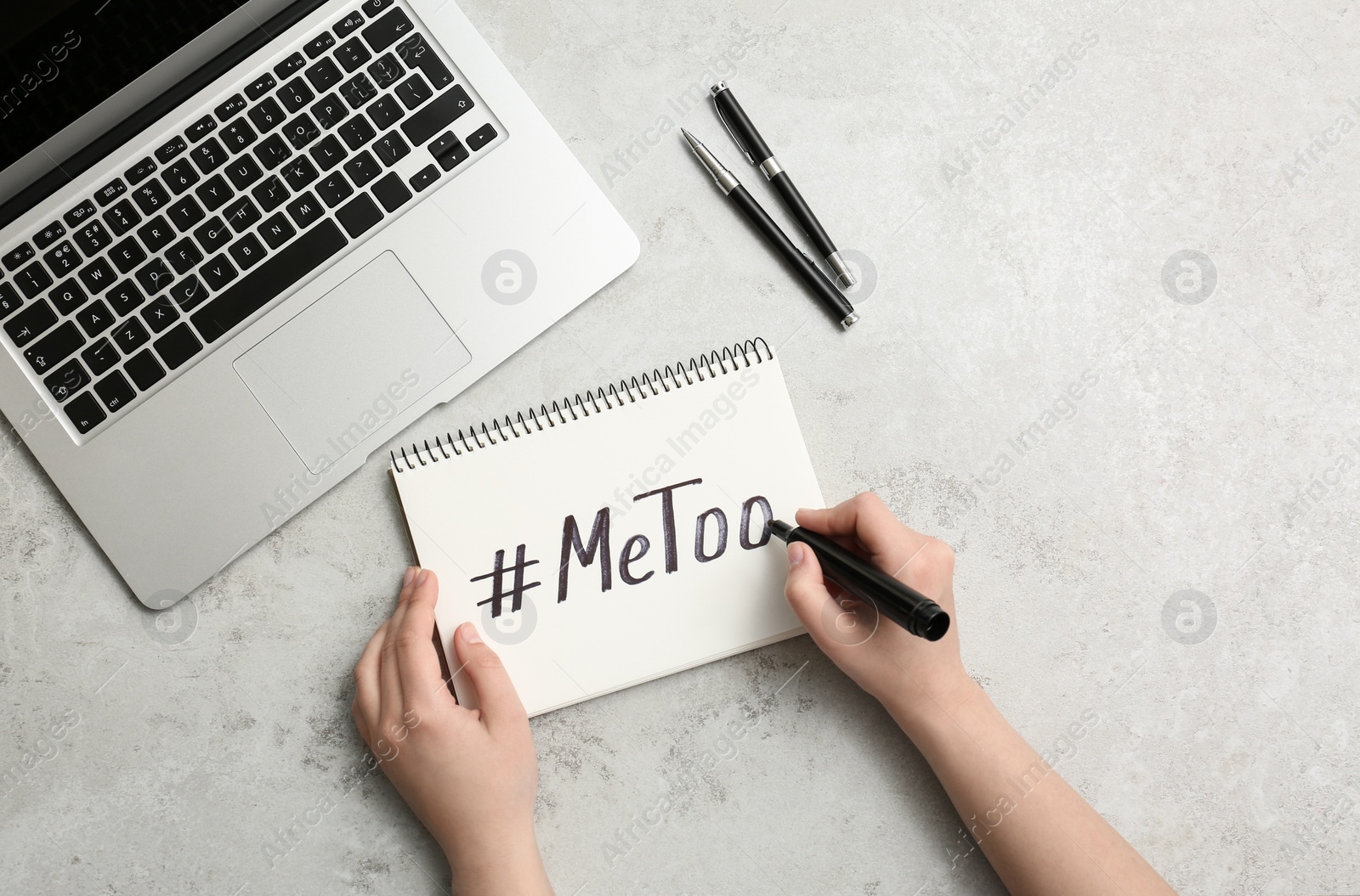 Photo of Woman writing hashtag METOO in notebook at grey table, top view. Stop sexual assault