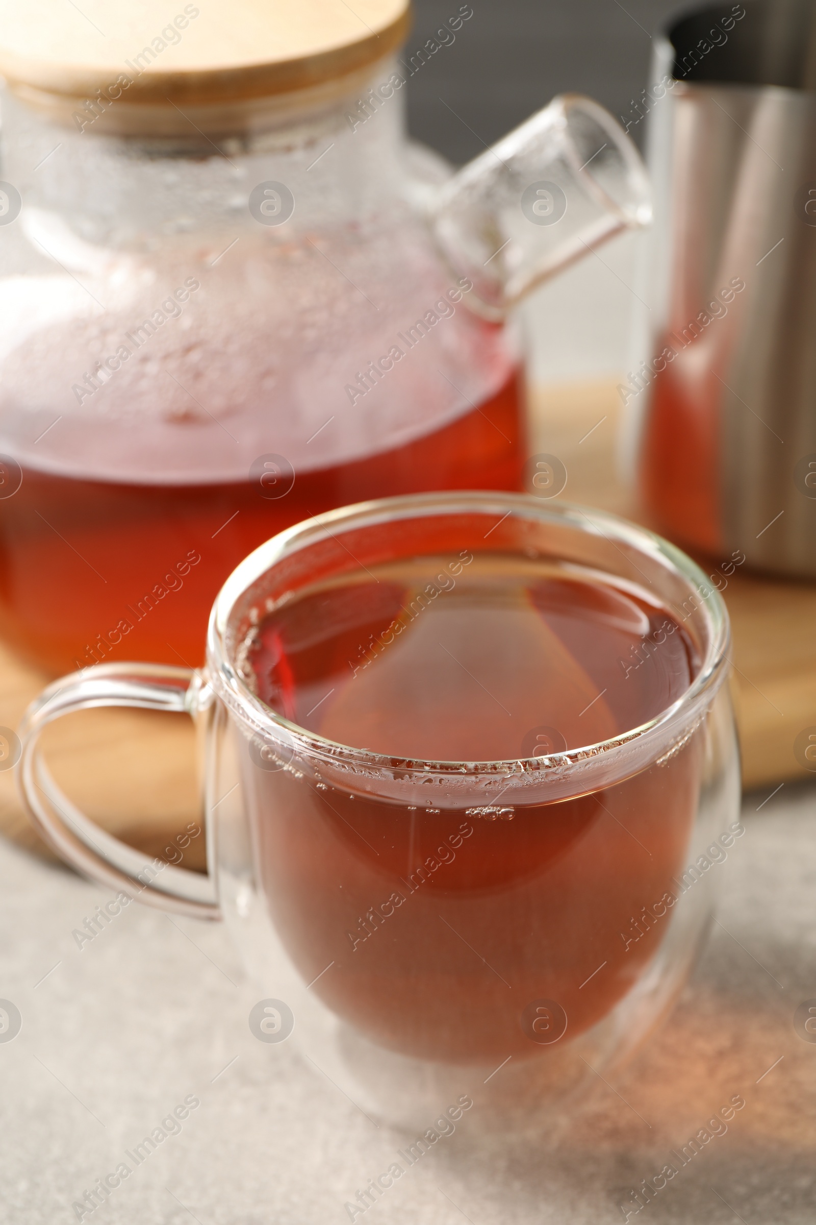 Photo of Aromatic tea in glass cup and teapot on light grey table, closeup