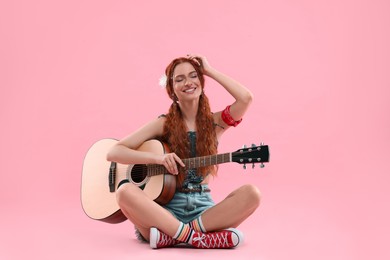 Stylish young hippie woman with guitar on pink background