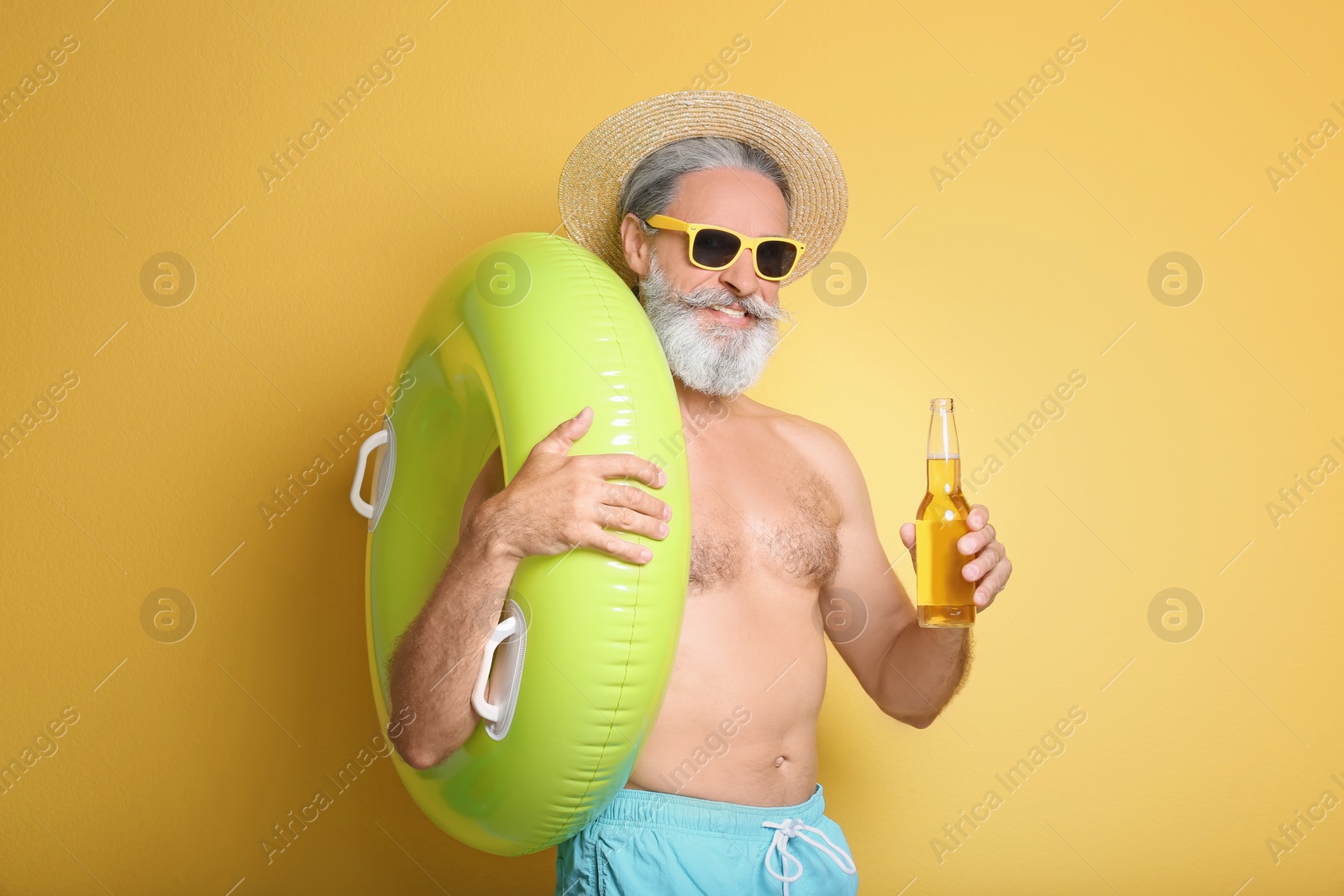 Photo of Shirtless man with inflatable ring and bottle of drink on color background