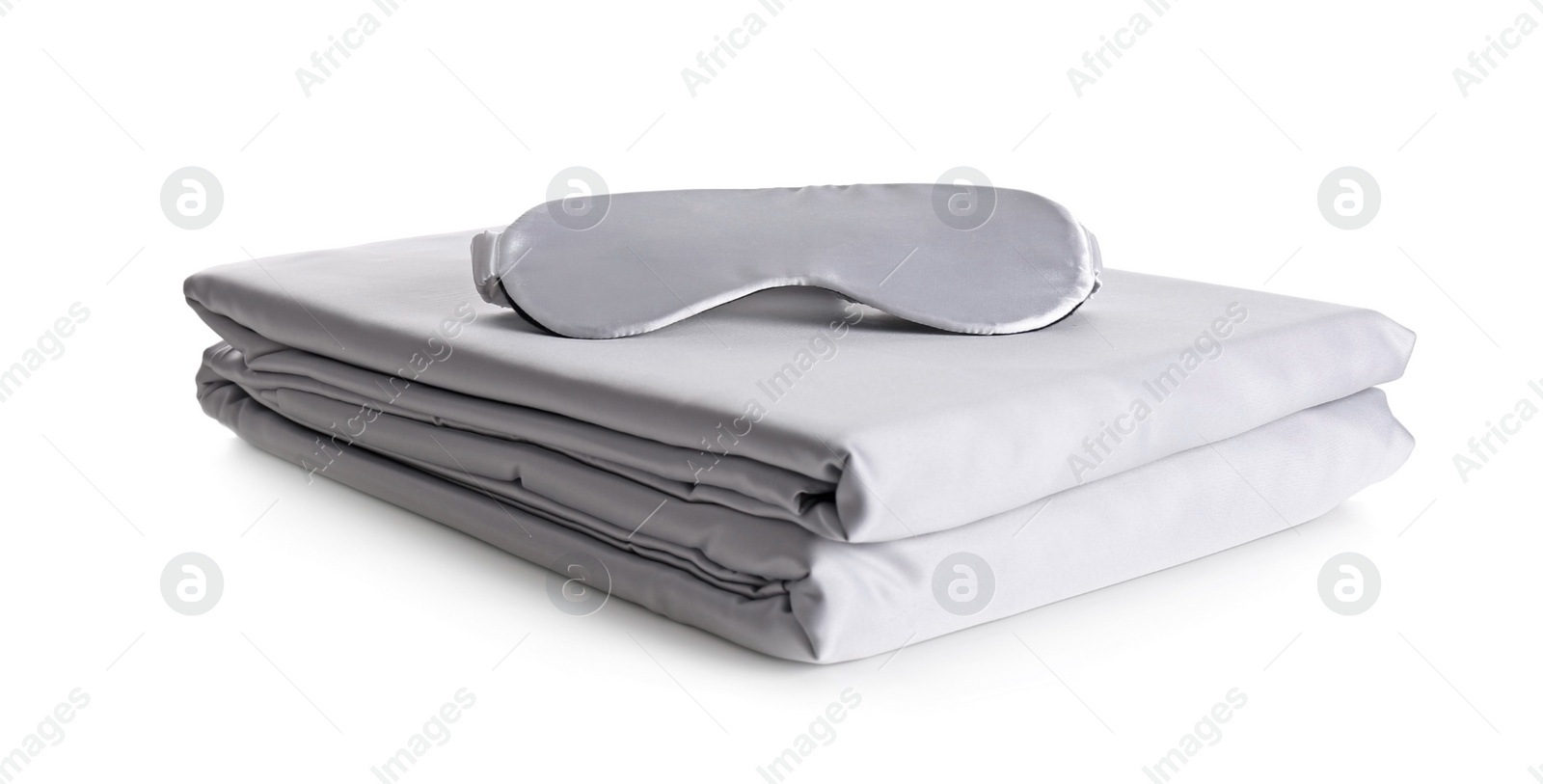 Photo of Stack of clean silky bed linen and sleeping mask isolated on white