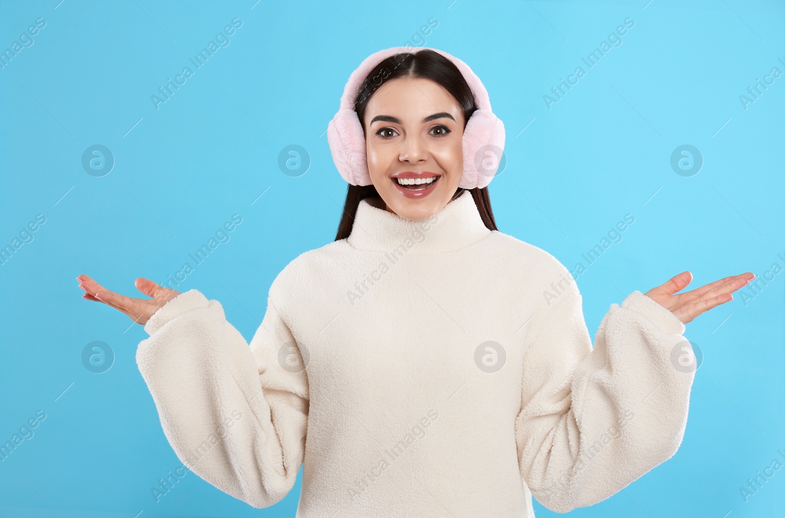 Photo of Beautiful young woman wearing earmuffs on light blue background