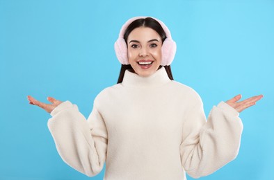 Beautiful young woman wearing earmuffs on light blue background