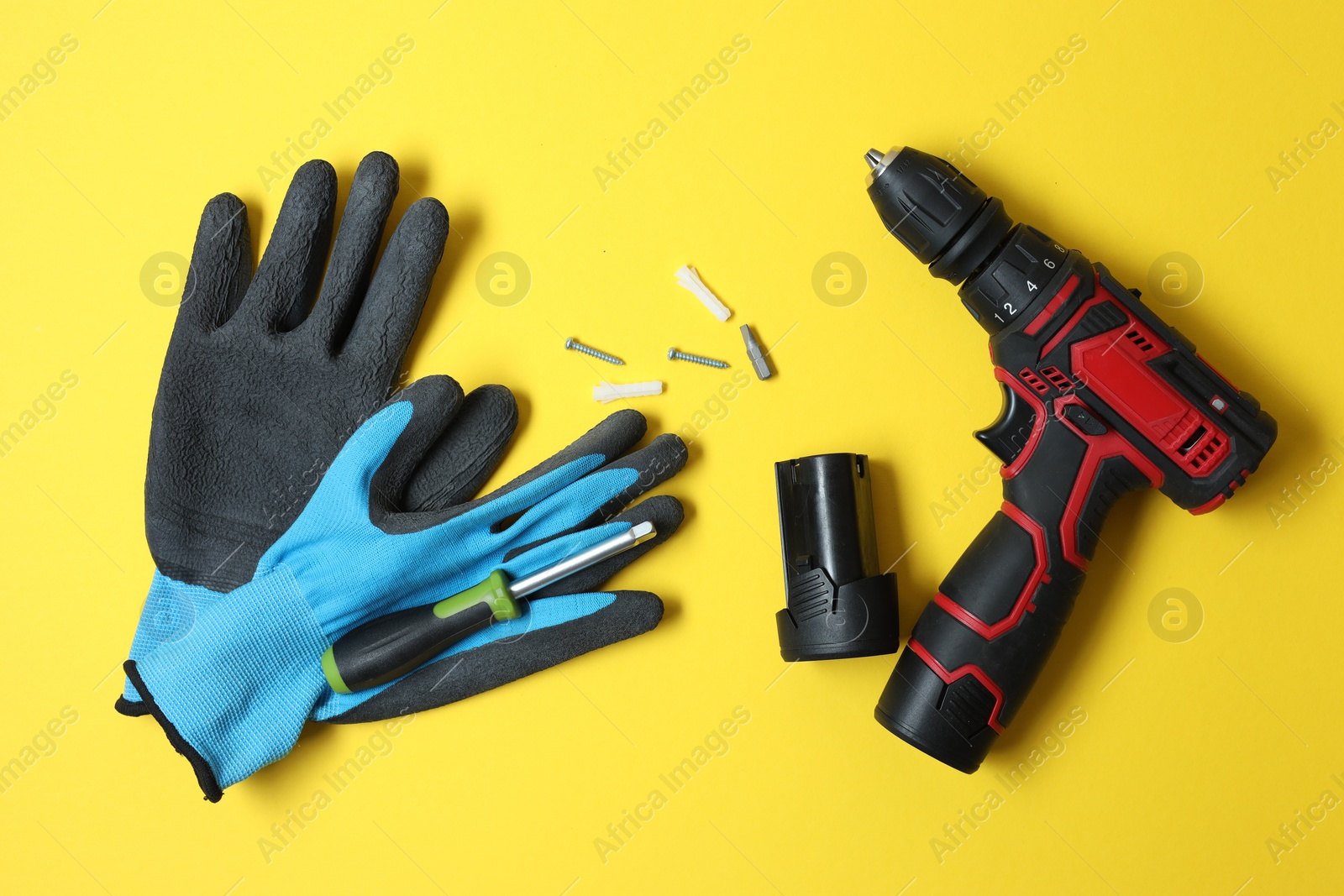 Photo of Electric screwdriver, bit set and gloves on yellow background, flat lay