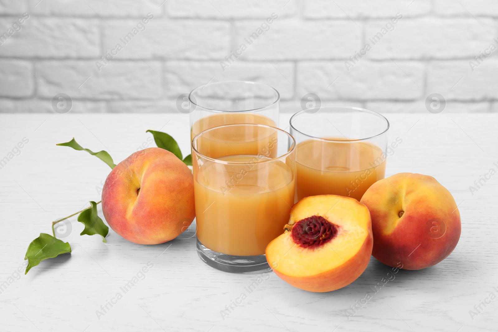 Photo of Glasses of delicious peach juice, fresh fruits and leaves on white wooden table