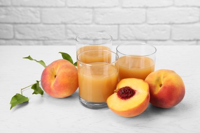 Photo of Glasses of delicious peach juice, fresh fruits and leaves on white wooden table