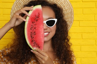 Photo of Beautiful young African-American woman with watermelon near yellow brick wall