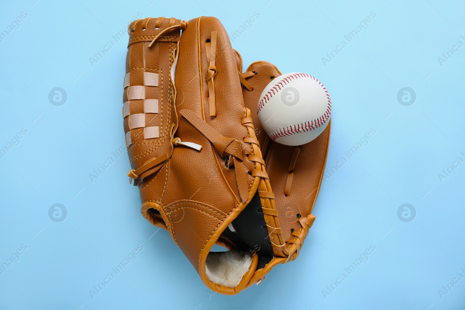 Photo of Catcher's mitt and baseball ball on light blue background, top view. Sports game