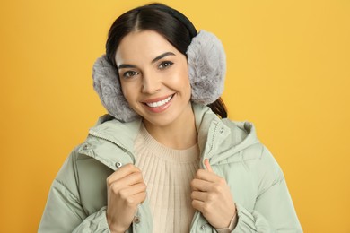 Photo of Beautiful young woman wearing earmuffs on yellow background