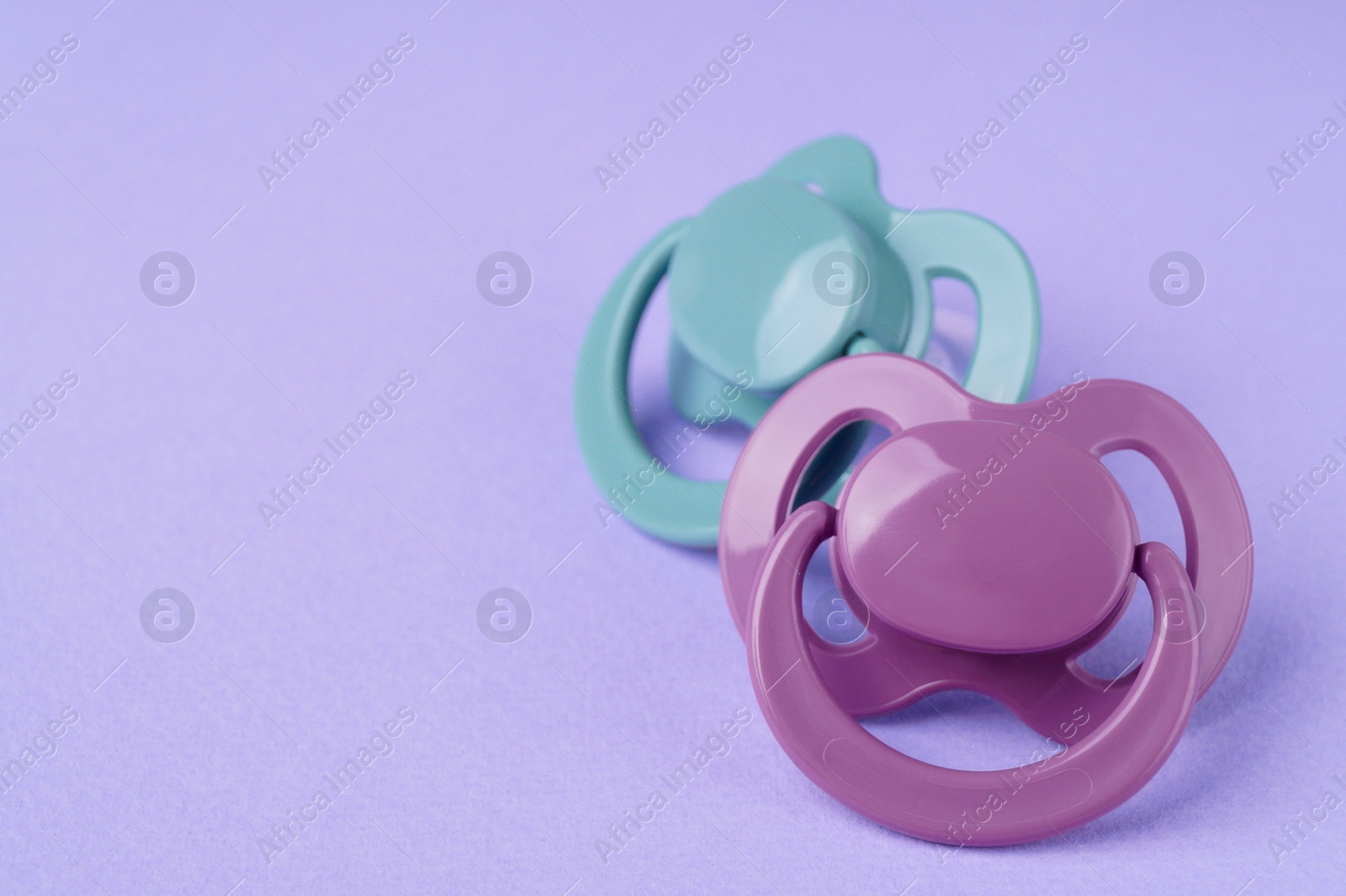 Photo of New baby pacifiers on purple background, closeup. Space for text