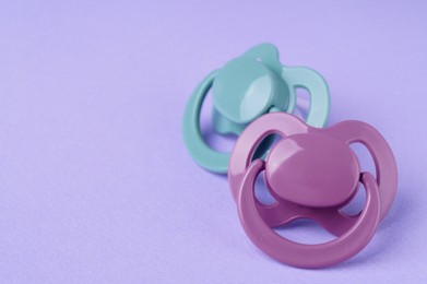 New baby pacifiers on purple background, closeup. Space for text