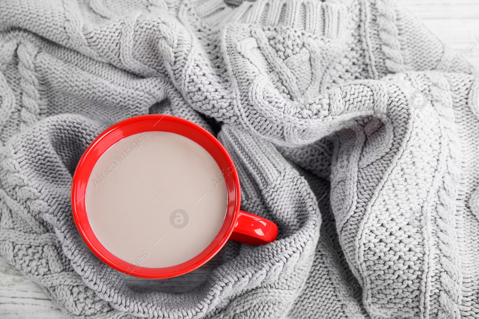 Photo of Cup of hot cocoa and knitted sweater on table, top view. Winter drink