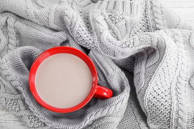 Photo of Cup of hot cocoa and knitted sweater on table, top view. Winter drink