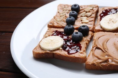 Different tasty toasts with nut butter and products on wooden table, closeup