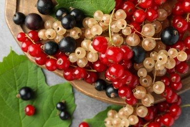 Photo of Different fresh ripe currants and green leaves on light grey table, top view