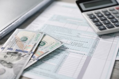 Photo of Payroll. Tax return forms, calculator and dollar banknotes on table, selective focus