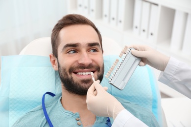 Dentist matching young man's teeth color with palette in office