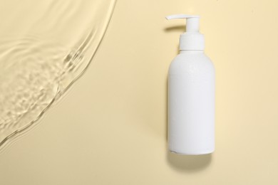 Photo of Bottle of face cleansing product in water against beige background, top view. Space for text