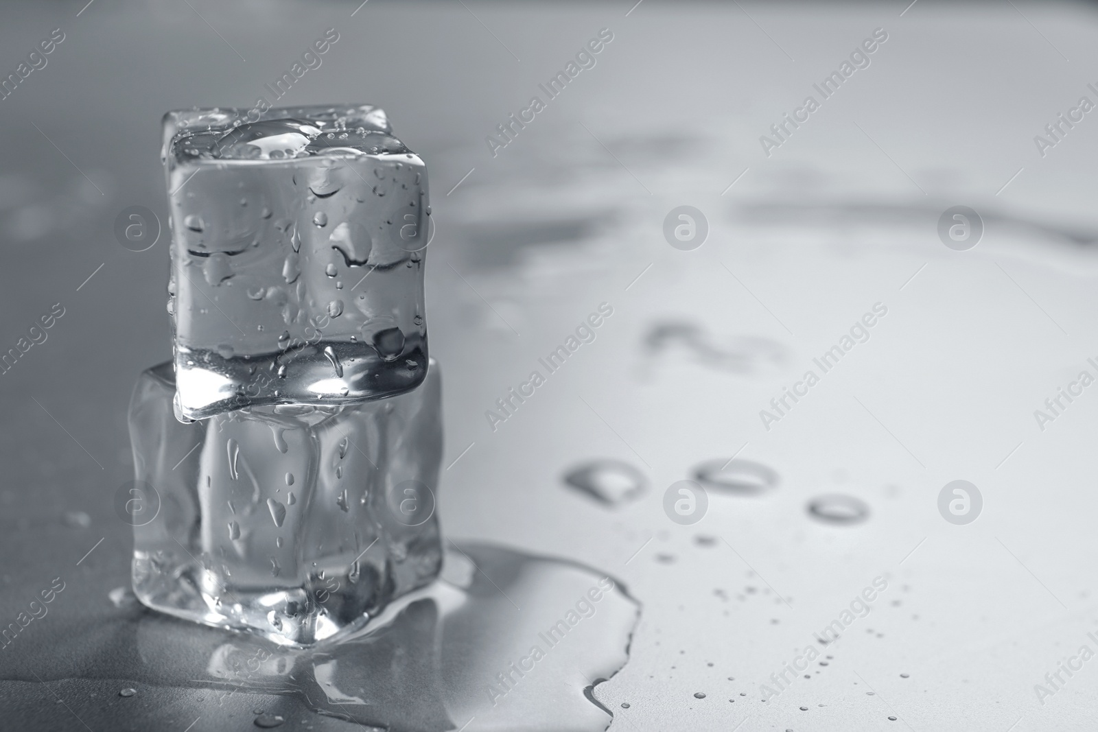 Photo of Crystal clear ice cubes with water drops on grey table, closeup. Space for text