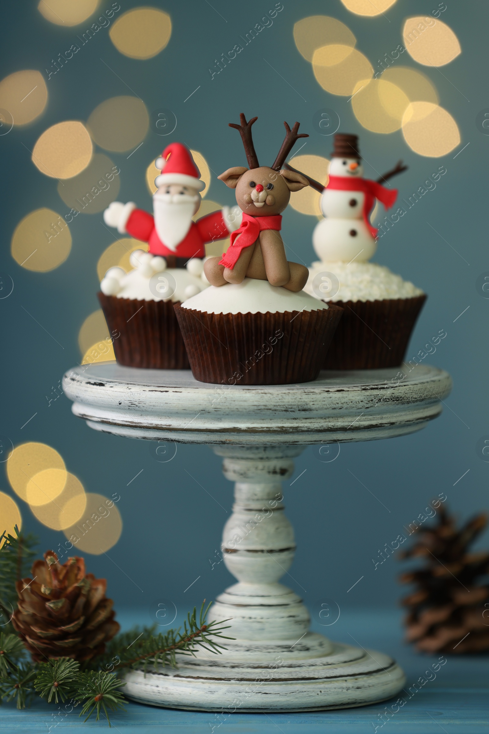 Photo of Tasty Christmas cupcakes on blue wooden table against blurred festive lights