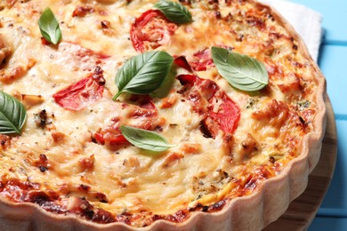 Photo of Tasty quiche with tomatoes, basil and cheese on light blue table, closeup