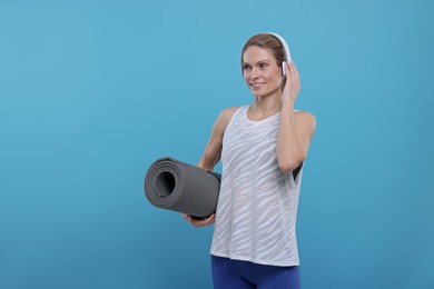 Sportswoman with headphones and fitness mat on light blue background, space for text