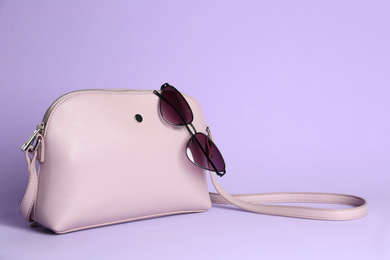 Stylish woman's bag and sunglasses on lilac background. Space for text