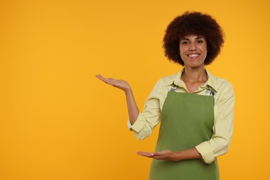 Photo of Portrait of happy young woman in apron on orange background. Space for text