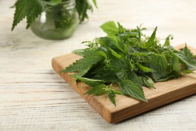 Photo of Board with fresh stinging nettle leaves on white wooden table, closeup