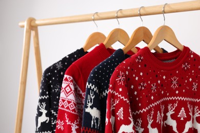 Different Christmas sweaters hanging on rack against light background, closeup