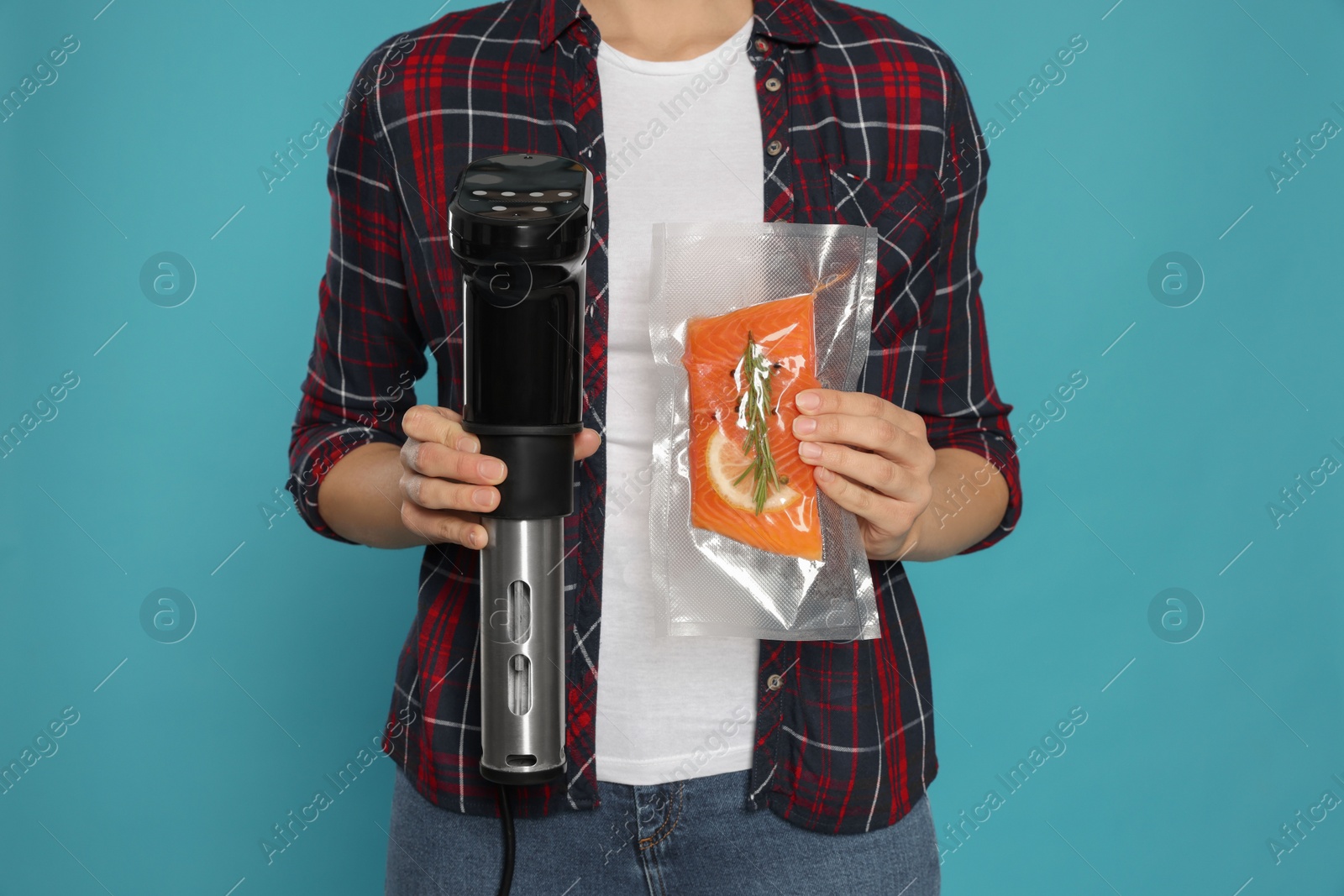 Photo of Woman holding sous vide cooker and salmon in vacuum pack on light blue background, closeup