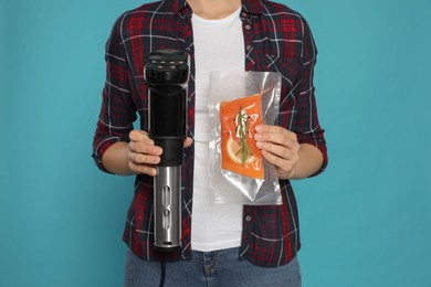 Photo of Woman holding sous vide cooker and salmon in vacuum pack on light blue background, closeup