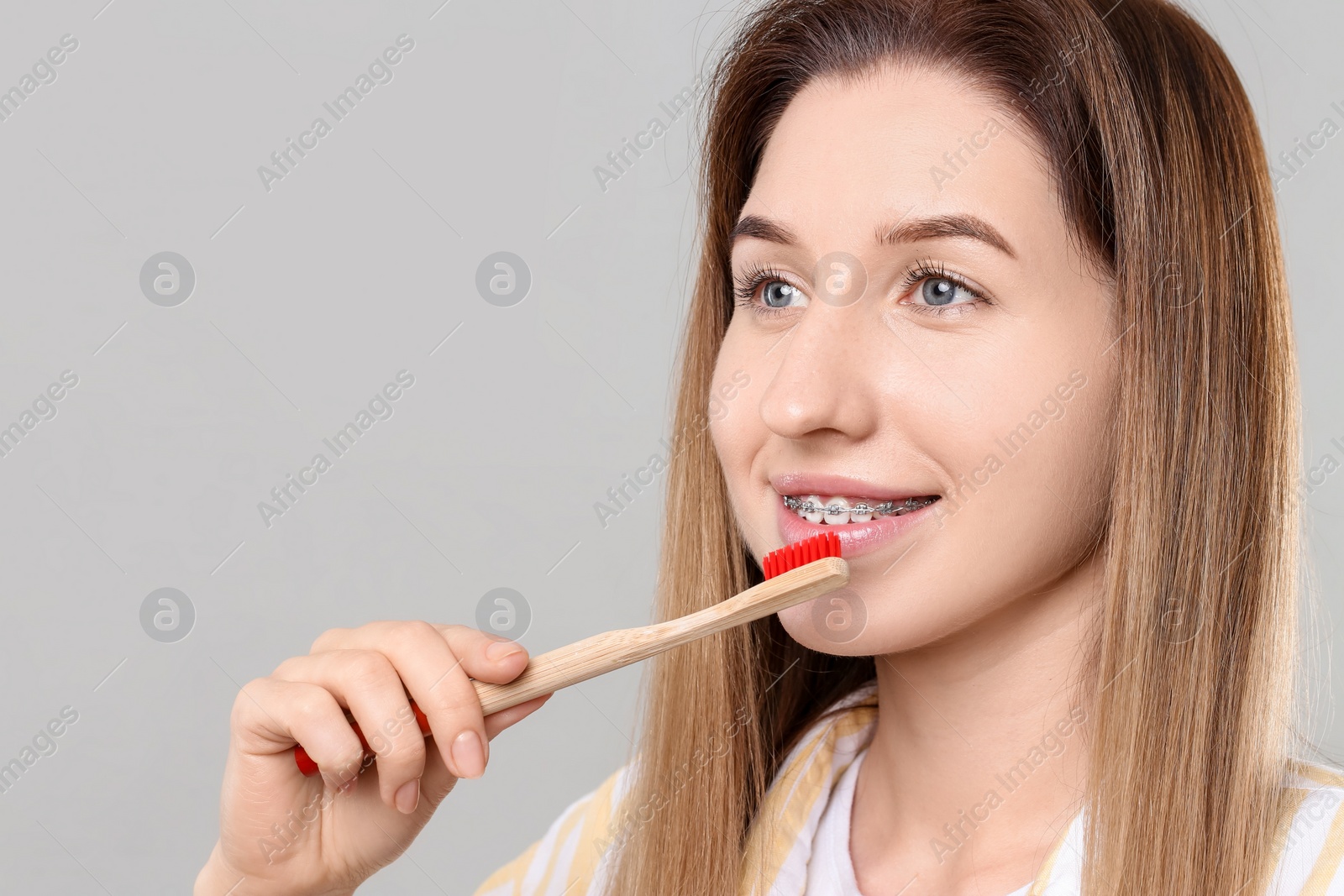 Photo of Smiling woman with dental braces cleaning teeth on grey background. Space for text