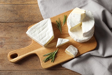 Wooden board with delicious cheeses on table, above view