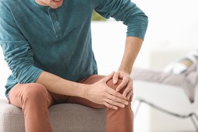 Photo of Young man suffering from knee pain at home