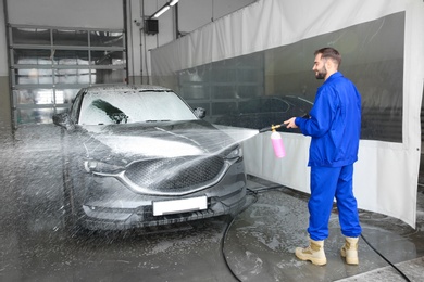 Worker cleaning automobile with high pressure water jet at car wash